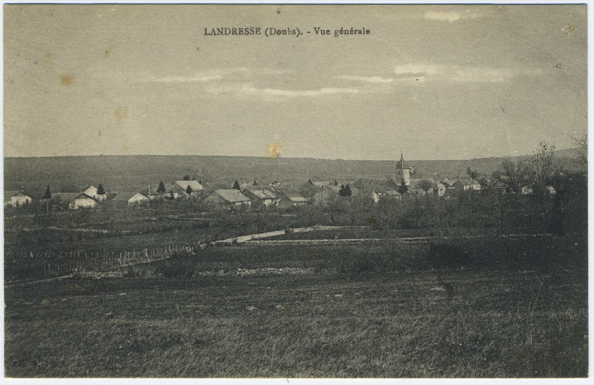 Carte postale ancienne en noir et blanc offrant une vue générale de Landresse (Doubs). Le village s'étire au loin dans un paysage de champs délimités par des haies, avec le clocher de l'église visible sur la droite.