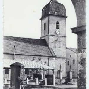 Carte postale ancienne verticale de la Place de l'Église à Landresse. L'image est cadrée depuis l'arche en pierre de la mairie, montrant une fontaine au premier plan et le clocher comtois en arrière-plan.