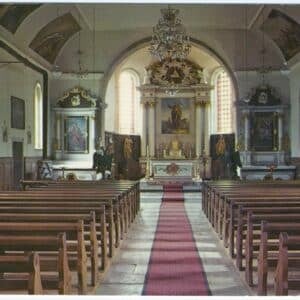 Photographie en couleur de l'intérieur de l'église de Landresse. L'allée centrale avec un tapis rouge sépare les bancs en bois et mène vers le chœur richement décoré d'autels baroques blancs et dorés sous une voûte peinte.